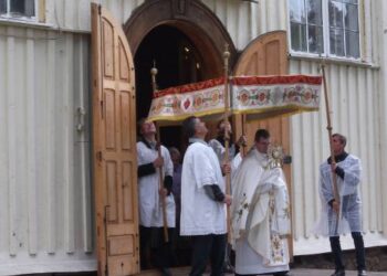 Rimti, iškilmių prasmę jaučiantys didžiąsias vėliavas nešantys procesijos vyrai.