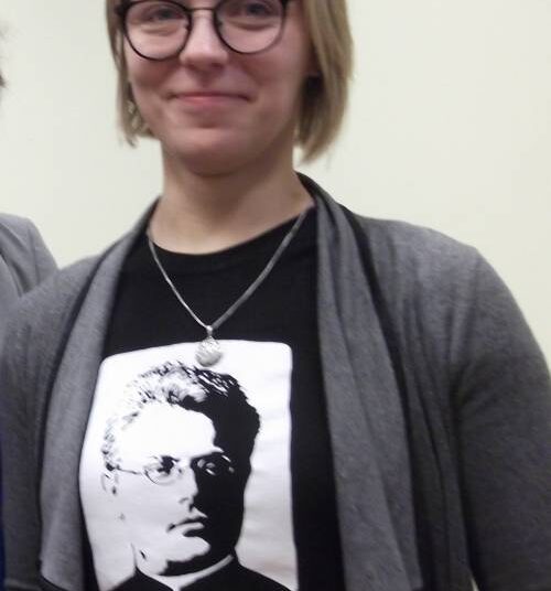Aistė Kučinskienė smagiai šypsosi – pasipuošusi Lietuvių kalbos ir literatūros instituto platinamais originaliais atributais – marškinėliais su Vaižganto atvaizdu ir citata: „Eikš ant blaivinančio pašnekesio“.